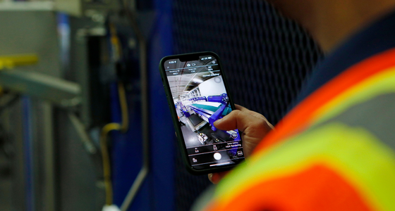 Worker holding a phone showing a short-form video on a plant floor